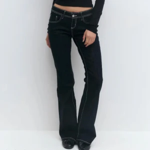 Mörkblåa bootcut jeans med kontrastsömmar - Snygga mörkblåa jeans från Gina Tricot med bootcut passform och låg midja. Jeansen har tydliga vita kontrastsömmar, klassiska fem fickor och stängs med knapp och dragkedja. Perfekta för en trendig och avslappnad look.