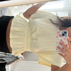 Ljusgul blus med volang och resår - Supersöt ljusgul blus med korta ärmar och bred resår i midjan som ger en volangig och luftig siluett. Perfekt för dig som gillar en feminin och trendig look. Tunt och skönt material som passar till många outfits.