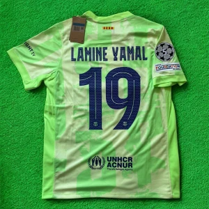 Barcelona Lamine Yamal fotbollströja - Snygg Barcelona fotbollströja med Lamine Yamal och nummer 19 på ryggen. Tröjan är ljusgrön med mönstrade detaljer, klubbmärke, Nike-logga och Champions League-patch på ärmen. Materialet är lätt och andas, perfekt för match eller träning.