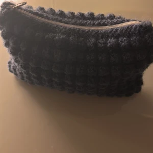 Mörkblå virkad necessär med dragkedja - Säljer en unik mörkblå virkad handväska med bubblig struktur och ljus dragkedja. Perfekt för att förvara småsaker eller smink. 