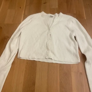 Vit ribbad kofta - Säljer en vit ribbad kofta med v-ringning och knappar framtill. Koftan är croppad och har långa armar. Enkel och stilren design som passar till det mesta. Fån Lindex i storlek 12-14 men passar XS.☺️🤩