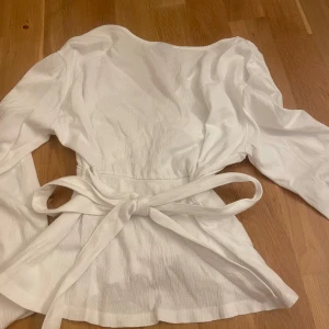 Vit blus med rosett i ryggen - Supersnygg vit blus från Gina Tricot med justerbar rosett knytning i ryggen. storlek XS. Toppen har långa ärmar, v-ringning framtil som ger en riktigt fin siluett. Perfekt gullig blus!!!🤩🤩