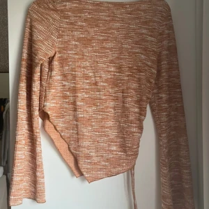 Orange mönstrad topp från Even&Odd -  orange och vit mönstrad topp från Even&Odd i återvunnen polyester. Modellen har lång ärm, asymmetrisk nederkant och  snörningsdetalj på sidan. Aldrig burit utan bara testad
