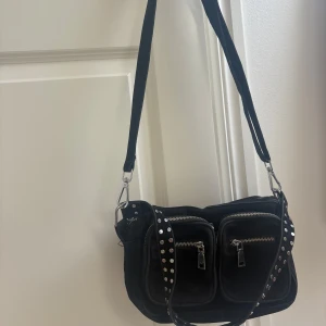 Svart axelväska från Noella - Svart Celia bag från Noella. Väskan är tillverkad av högkvalitativ konstläder. Denna väska har flera fack med blixtlås så man får plats med mycket och en justerbar axelrem så man kan ha den så som man vill själv.   Väskan är i jättebra skick, använts få gånger och köptes helt ny.