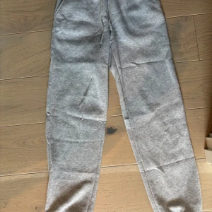 Grå mjukisbyxor med snörning - Snygga grå mjukisbyxor med dragsko i midjan och avslappnad passform. Perfekta för chill dagar eller när du vill vara bekväm. Tillverkade i mjukt bomullsmaterial och har klassisk look utan tryck eller mönster.