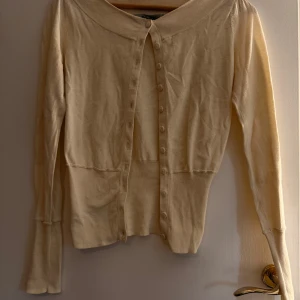 Beige kofta från Noa Noa i bomull - Supersöt beige kofta från Noa Noa i mjuk bomull. Klassisk modell med rund halsringning, långa ärmar och täckta knappar framtill. Perfekt att slänga över en topp eller klänning för en chill och stilren look.