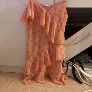 Ljusrosa långklänning med volanger - Säljer en superfin ljusrosa långklänning från C i storlek 146. Klänningen har tunna axelband, volangdetaljer och ett blommigt mönster i samma ton. Materialet känns lätt och flowy, perfekt för varma dagar. Volangerna ger en extra touch av romantisk vibe.