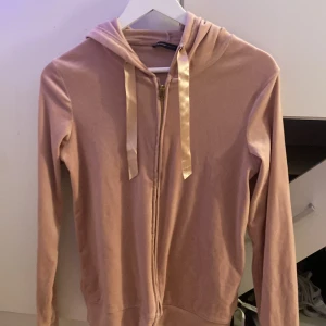 Rosa hoodie med dragkedja från mywear woman - Mjuk rosa hoodie från mywear woman i storlek XS. Tröjan har huva med breda satinband, guldig dragkedja framtill och långa ärmar. Perfekt för en chill och avslappnad stil. Materialet känns lent och bekvämt mot huden.