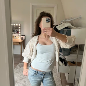 Vit/beige spetskofta med knappar - Säljer en söt vit/beige kofta med spetsdetaljer och knappar framtill. Koftan är stickad med ett vackert mönster och har långa ärmar.💘Perfekt att slänga över ett linne för en romantisk look.💘🤩