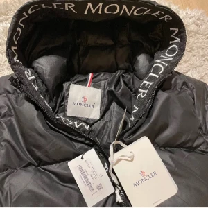 Svart dunjacka från Moncler - Säljer en svart lång dunjacka från Moncler med huva ,Jackan har Moncler-logga på huvan. Aldrig använd.