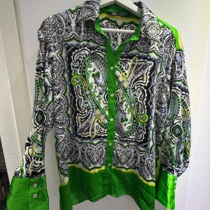 Mönstrad skjorta med gröna detaljer från Zara - Säljer en färgstark skjorta från Zara med gröna, svarta och vita mönster samt paisley-detaljer. Skjortan har långa ärmar, knappar framtill och en klassisk krage. Perfekt för dig som vill sticka ut med din stil!