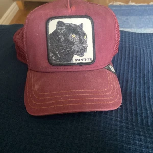 Vinröd keps med pantermärke från The Farm - Vinröd keps med broderad patch av en svart panter framtill. Kepsen har böjd skärm, mesh baktill och justerbar passform. Märkt med The Farm på insidan. Perfekt för en cool och avslappnad stil.