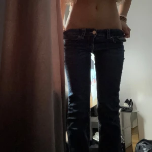 Mörkblå lågmidjade bootcut jeans - Säljer ett par mörkblå jeans med låg midja och klassisk femficksdesign. Jeansen har raka ben och tydliga sömmar på bakfickorna. Perfekta för dig som gillar en avslappnad och tidlös stil. Har ett litet hål precis vid fickan men det är sytt!
