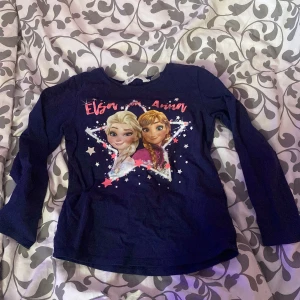 Mörkblå långärmad tröja med Elsa och Anna från H&M - Säljer en mörkblå långärmad tröja från H&M med motiv av Elsa och Anna från Disney Frost. Tröjan har tryck med stjärnor och text framtill. Perfekt för alla Frost-fans!