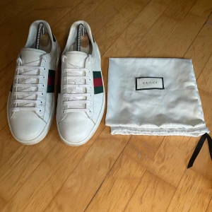 Gucci ace sneakers med gröna och röda detaljer - Säljer ett par snygga Gucci Ace skor i storlek 9 vilket motsvarar ca 43-44. De är väl använda men har mycket kvar att ge. Skorna har snörning och medföljer original dustbag. Perfekta för dig som vill ha en stilren och lyxig look. Obs. Inga byten. Hör av er vid funderingar!