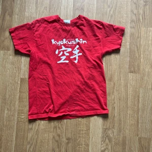 Röd Kyokushin t-shirt från Fruit of the Loom - Röd t-shirt från Fruit of the Loom med vit text och japanska tecken på bröstet, relaterad till Kyokushin karate. Klassisk passform och rund hals. Perfekt för träning eller vardag.