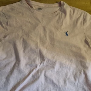 Ljusrosa t-shirt från Polo Ralph Lauren - Ljusrosa t-shirt från Polo Ralph Lauren med klassisk passform och blå broderad logga på bröstet. Tillverkad i mjuk bomull och har korta ärmar. Perfekt basic att ha i garderoben.