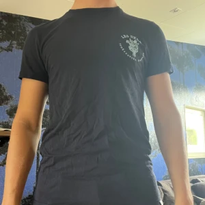 Mörkblå t-shirt - Säljer en mörkblå t-shirt från Les Deux med liten vit logga och text på bröstet. Klassisk passform och rund halsringning. Perfekt för en stilren och enkel look. Normal i passform och mkt bra skick 🤩