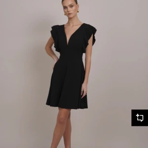 Svart cocktailklänning - Supersnygg svart klänning med djup v-ringning och volangdetaljer vid axlarna. Hör av dig vid intresse🫶