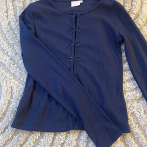 mörkblå topp - Jag säljer en mörkblå topp ifrån Nelly, materialet på toppen är ribbat och har rosetter fram till. Storleken är s och toppen är använd en gång. 