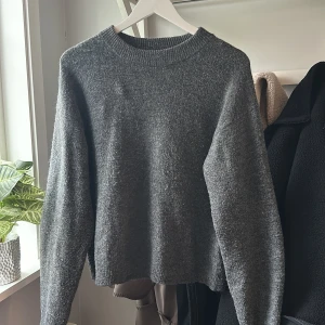 Grå stickad tröja från H&M - Mysig grå stickad tröja från H&M med rund halsringning och ribbade muddar. Perfekt för kyliga dagar och enkel att matcha med olika outfits. Klassisk och stilren modell som passar till det mesta.