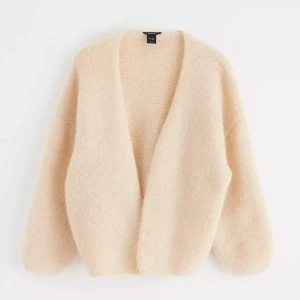 Lindex kofta - Mysig och fluffig beige kofta med öppen front och långa ärmar. Perfekt att slänga på sig över en t-shirt eller klänning för en avslappnad och stilren look. Koftan har en lös passform och är superbekväm passar perfekt inför sommarkvällar 