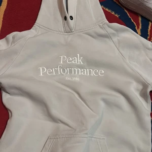 Beige hoodie från Peak Performance - Säljer en ljusgrå  hoodie från Peak Performance med broderad logga på bröstet. 
