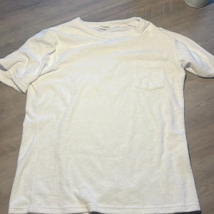 Vit t-shirt med bröstficka från John Henric - Säljer en klassisk vit froté t-shirt från John Henric i 100% bomull. T-shirten har korta ärmar och en liten bröstficka på vänster sida. Perfekt basic-plagg till garderoben.