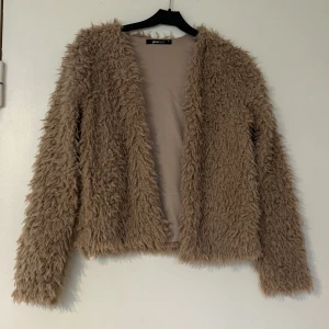 Beige fluffig jacka från Gina Tricot - Säljer en supermjuk och fluffig beige jacka från Gina Tricot. Jackan har lång ärm och är tillverkad i ett pälsliknande syntetmaterial. Väldigt bra skick har bara använd fåtal gånger 