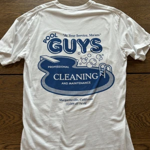 Vit t-shirt med blått tryck från Vailent - Vit t-shirt från Vailent med blått tryck på bröstet och stort tryck på ryggen med texten 'Pool Guys Professional Cleaning'. Storlek S med någorlunda oversize passform. Passar S/M. 