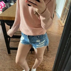 Blå jeansshorts med fransar - Snygga blå jeansshorts med slitna detaljer och fransar längs bensluten. Klassisk femficksmodell med knapp och dragkedja framtill. Perfekta för varma dagar och enkel att matcha med olika toppar.