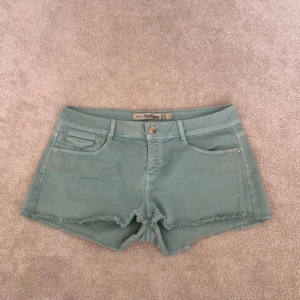Turkosa jeansshorts från Zara - Säljer ett par ljusgröna jeansshorts från Zara med fransad kant nertill. Shortsen har klassisk femficksdesign, bälteshällor och knappgylf. Perfekta för varma dagar och enkel att matcha med olika toppar.skulle säga att de inte är som en storlek l utan mer åt m 
