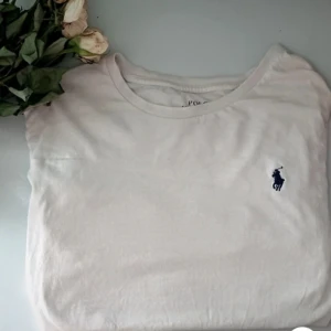 Vit t-shirt från Polo Ralph Lauren - Vit klassisk t-shirt från Polo Ralph Lauren med rund halsringning och den ikoniska broderade loggan i mörkblått på bröstet. Perfekt basic-plagg i mjuk bomull som passar till allt.