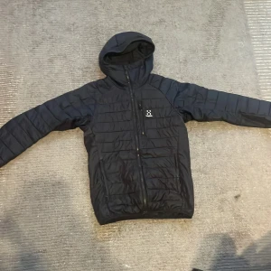 Svart pufferjacka från Haglöfs med huva - Säljer en svart pufferjacka från Haglöfs, modell Spire Mimic Hood Men. Jackan har huva, dragkedja framtill och en bröstficka med dragkedja. Perfekt för kyliga dagar och har en sportig look.