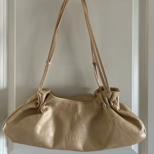 Beige axelväska från FERCHI - Snygg beige axelväska från FERCHI i skinn med dubbla axelband och dragkedja upptill. Väskan har ett huvudfack och innerficka med dragkedja. Den är i väldigt fint skick knappt använd 