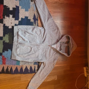 Ljusgrå hoodie från Weekday - Säljer en ljusgrå hoodie från Weekday med dragkedja framtill och två fickor. Tröjan har huva och är långärmad, perfekt för en avslappnad stil. Passar dig som gillar enkel och stilren design.