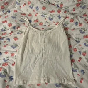 Vit topp från Brandy Melville - Säljer en enkel och stilren vit topp från Brandy Melville. Toppen har tunna axelband och är tillverkad i mjuk bomull, perfekt för varma dagar eller som lager under andra plagg 🫶🏼🫶🏼