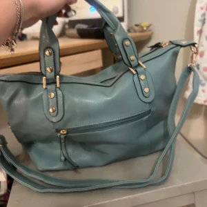 Ljusblå axelväska - Snygg ljusblå axelväska med både handtag och justerbar axelrem. Väskan har guldfärgade metalldetaljer, dragkedja upptill och en praktisk ytterficka med dragkedja. Perfekt storlek för vardagens alla prylar. Väskan är från Amazon och nypris är 450 kr + frakt. Har tyvärr inte kommit till användning och prislappen är kvar.💕