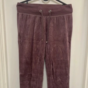 Lila mjukisbyxor med dragsko - Säljer ett par lila mjukisbyxor med bred resår och dragsko i midjan. Byxorna är i ett mjukt, sammetsliknande material och har muddar vid bensluten. Perfekta för en avslappnad stil.