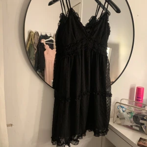 Svart prickig klänning med volangdetaljer - Säljer en svart klänning med tunna axelband och v-ringning. Klänningen har små prickar i tyget, jätte fin till sommaren, i storlek M men passar S! Hör av er vid frågor❤️❤️❤️.