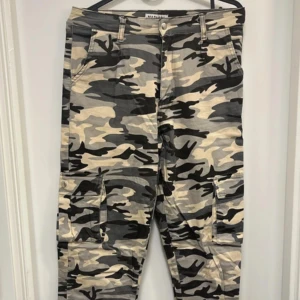 Cargobyxor i camouflage från Madlady - Säljer ett par cargobyxor från Madlady med klassiskt camouflage-mönster i beige, svart och grått. Byxorna har flera fickor på sidorna och resår vid bensluten. Perfekta för en streetwear-look.
