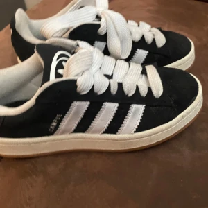 Svarta Adidas Campus sneakers med vita ränder - Säljer ett par klassiska Adidas Campus sneakers i svart mocka med vita ränder och vit sula. Köptes för en månad sen använt typ 3 gånger dome som helt ny ba lite smutsiga