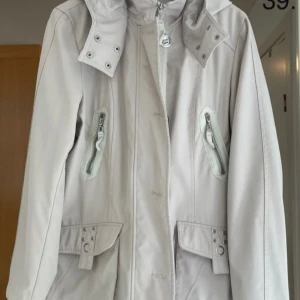 (Nr 39) KappAhl. Elegant kappa. Dam. Stl: M, 40/42. - Elegant kappa från KappAhl i beige färg till dam i storlek medium (40/42). Kappan är fodrad med innertyg, passar bäst för vår och höst. Jackan har fina detaljer och flera fickor på utsidan samt en innerficka. Luvan på jackan är rejält tilltagen och skyddar väl när det är kallt och blåser. Luvan är dessutom en avtagbar luva. Både dragkedja samt knäppning på jackan för att effektivt stänga ute kalla vindar. Finns i ett djurfritt och rökfritt hem. Sparsamt använd och i mycket fint skick.
