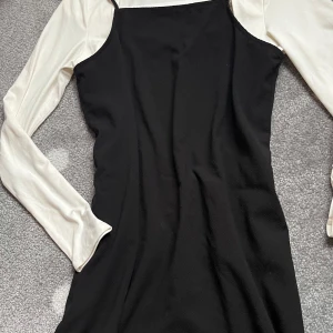 Svart klänning med vita långärmade ärmar - Säljer en svart klänning med smala axelband och vita långärmade tröja. Klänningen har en rak passform och är perfekt för dig som gillar en stilren och trendig look. Passar en xs. Tröjan är strl S. Enkel att styla med sneakers eller boots.