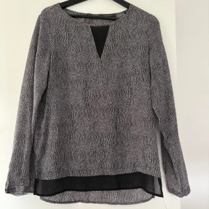 Svartvit blus från Esprit med transparent detalj - Säljer en svartvit mönstrad blus från Esprit med lång ärm och snygg transparent kant nertill. Blusen har en liten v-ringning framtill och är tillverkad i ett lätt, luftigt material. Perfekt för dig som gillar stilrena och unika detaljer.