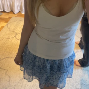 Blå blommig volangkjol - Supersöt blå kjol med blommigt mönster och volangdetaljer. Kjolen är kort och har en luftig känsla, perfekt för varma dagar. Resår i midjan för skön passform. Passar dig som gillar en feminin och somrig stil.