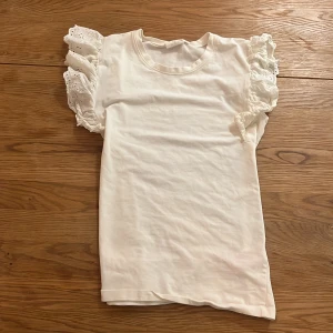 Vit topp med volangärmar från THE NEW - Supersöt vit topp från THE NEW med korta ärmar och breda volanger i spets. Mjuk bomullskänsla och rund halsringning. Även inte mycket använd men kommer tvättas innan jag skickar💕