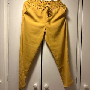 Gula byxor från Zara - Säljer ett par gula mjuka byxor från Zara med resår och snörning i midjan. Byxorna har en avslappnad passform och är perfekta för en chill stil. Fickor på sidorna och mjukt material gör dem extra bekväma.