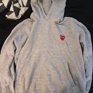  Comme des Garçons Play hoodie - Säljer en grå hoodie från Comme des Garçons Play med det klassiska röda hjärtat med ögon broderat på bröstet. Tröjan har huva och en stor magficka framtill. Perfekt för en avslappnad och stilren look. Priset är inte satt i sten och kan diskuteras vid snabb affär!