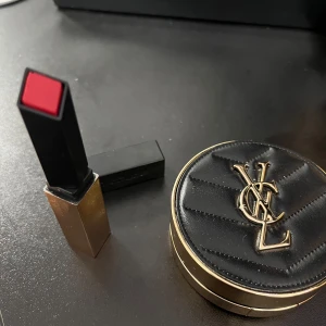 YSL läppstift och cushion foundation - Säljer ett lyxigt rött läppstift med fyrkantig hylsa och en svart-guldig cushion foundation med YSL-logga. Foundationen har spegel och applikator med logotyp. Perfekt för dig som gillar exklusivt smink och snygg design.